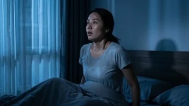 Một người phụ nữ giật mình tỉnh giấc giữa đêm vì ác mộng với khuôn mặt lo âu và đổ mồ hôi