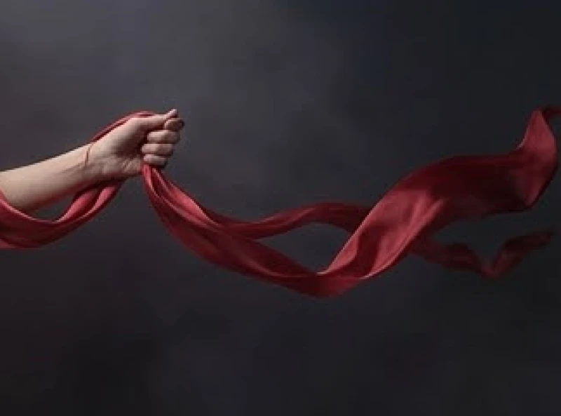 Bàn tay nắm chặt một dải lụa đỏ bồng bềnh trôi dạt giữa không trung u tối huyền bí