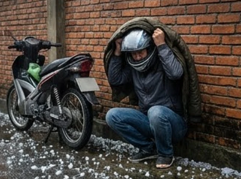 Người điều khiển xe máy đang khom người đội mũ bảo hiểm và lấy áo che gáy để trú bão