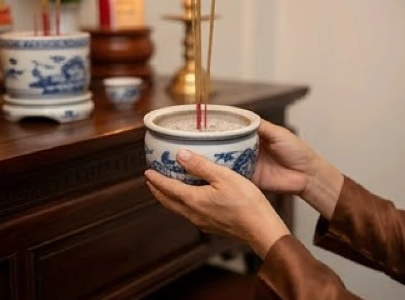 Đôi tay cẩn trọng nâng bát hương gốm sứ đặt lên khay để chuẩn bị di chuyển sang vị trí thờ cúng mới