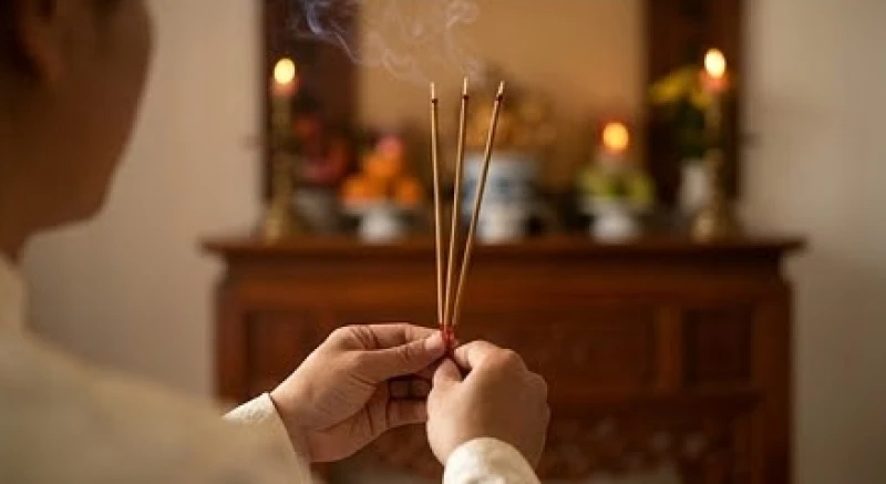 Bàn tay nâng nén hương đỏ rực ngang tầm mắt một cách trang nghiêm trước khi cắm vào bát nhang trên ban thờ