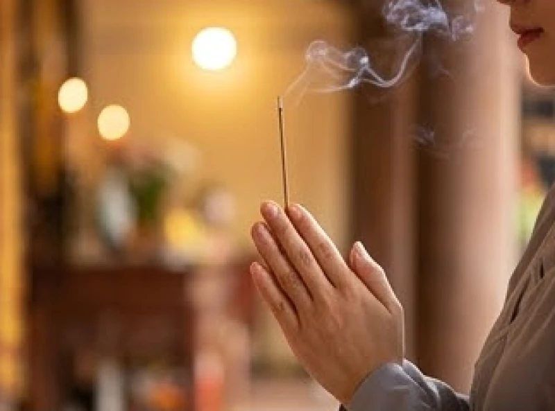 Hai bàn tay chắp hình búp sen kẹp nén nhang trầm đang tỏa khói mờ ảo trong ánh sáng huyền bí của chánh điện