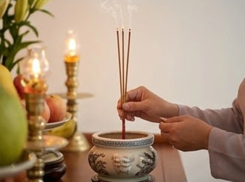 Người chủ lễ dùng hai tay cẩn thận cắm ba nén hương đang cháy vào bát hương chính giữa bàn thờ