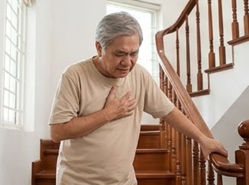 Người lớn tuổi ôm ngực trái nhăn mặt vì cơn đau thắt ngực bất ngờ khi đang leo cầu thang trong nhà