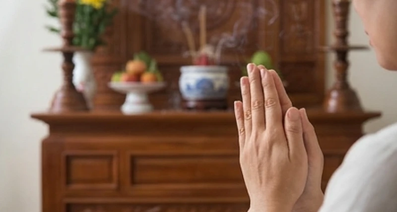 Một người đang thành tâm chắp tay khấn vái trước bàn thờ gia tiên nghi ngút khói nhang