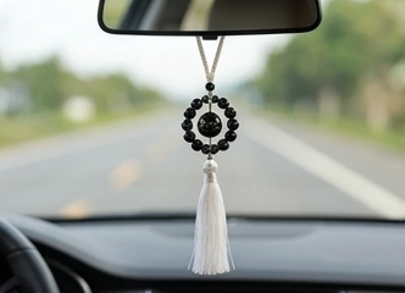 Dây khánh treo phong thủy tết từ các hạt đá obsidian đen và tua rua trắng đung đưa dưới gương chiếu hậu xe