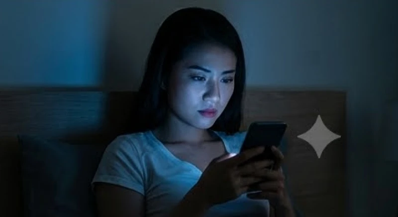 Người phụ nữ cầm màn hình điện thoại phát sáng giữa bóng tối của phòng ngủ