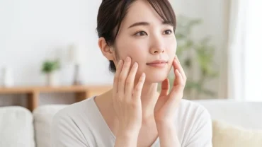 Người phụ nữ Á Đông đang chạm tay nhẹ lên vùng gò má trái để cảm nhận hiện tượng má trái giật là điềm gì.