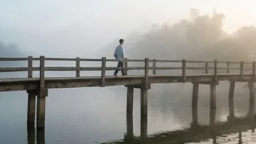 Một người thong thả bước trên cây cầu gỗ vững chãi trong mây mờ ảo tái hiện lại giấc mơ thấy đi qua cầu