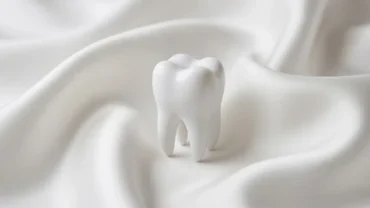 Chiếc răng trắng sáng đặt trên nền vải mềm mại tượng trưng cho giấc mơ thấy gãy răng không chảy máu an lành
