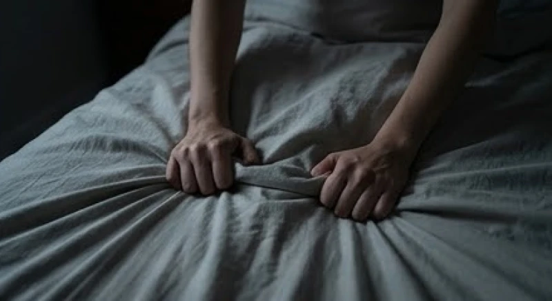 Bàn tay nắm chặt ga giường trong không gian phòng tối mờ thể hiện sự căng thẳng
