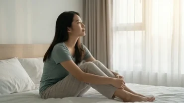 Người phụ nữ thức giấc trầm tư trên giường ngủ phản ánh trạng thái tâm lý khi mơ thấy mình bị ung thư