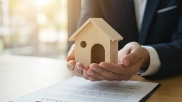 Người đàn ông cầm mô hình ngôi nhà nhỏ trên tay với vẻ mặt trầm tư khi nghĩ về giấc mơ mua bán nhà đất