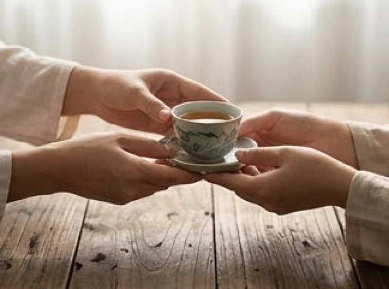 Hai bàn tay đang trao nhau chén trà ấm áp thể hiện sự tương trợ và mượn tuổi trong phong thủy