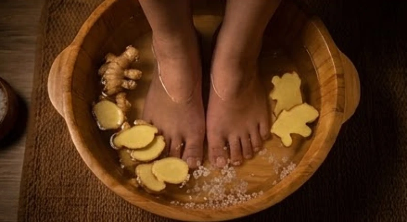 Đôi bàn chân đang được ngâm trong chậu nước ấm pha với muối hạt và gừng thái mỏng