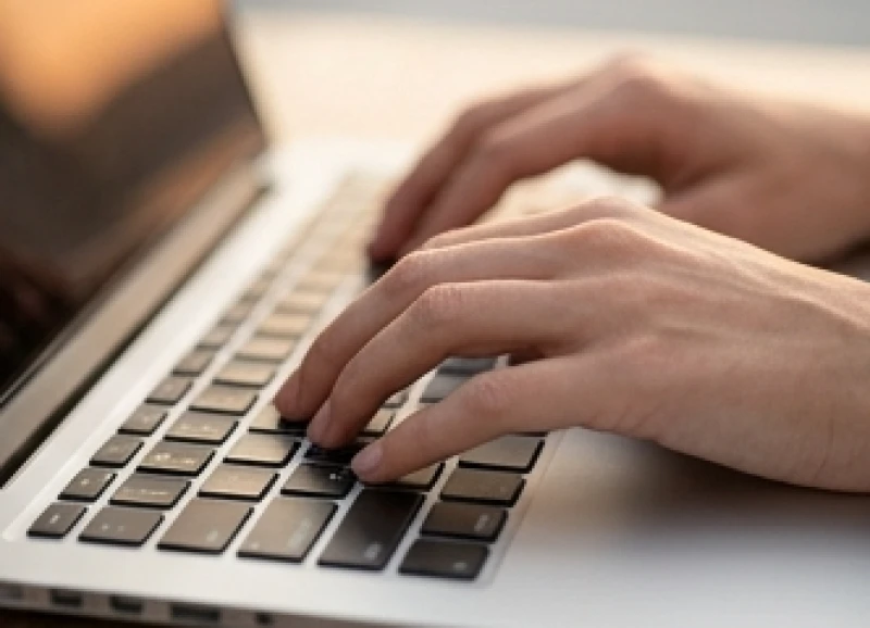 Bàn tay gõ bàn phím laptop với những ngón tay thon dài di chuyển cẩn trọng trên từng phím bấm