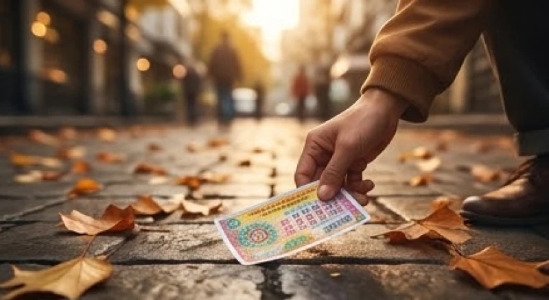Bàn tay nhặt một tờ vé số rơi trên vỉa hè đầy lá vàng dưới ánh đèn đường