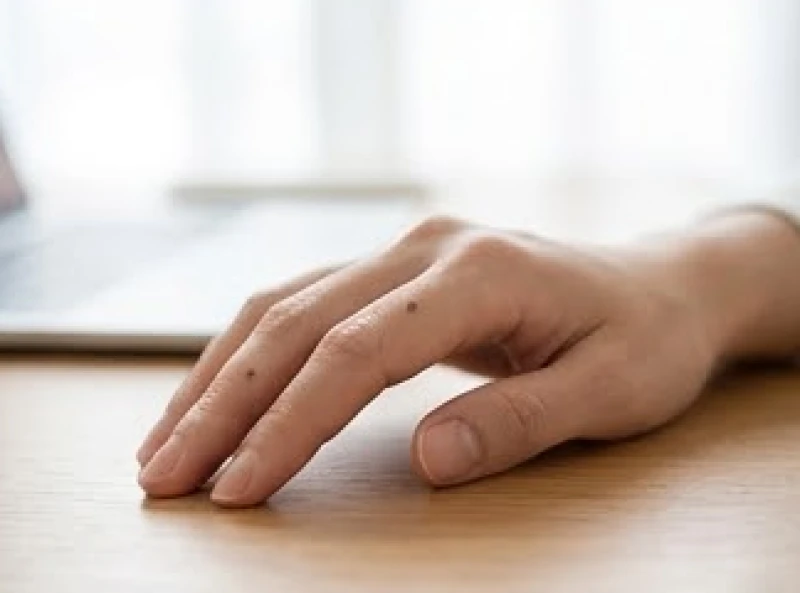 Bàn tay đặt nhẹ nhàng lên bàn làm việc với nốt ruồi nhỏ mọc ngay trên đốt ngón tay giữa