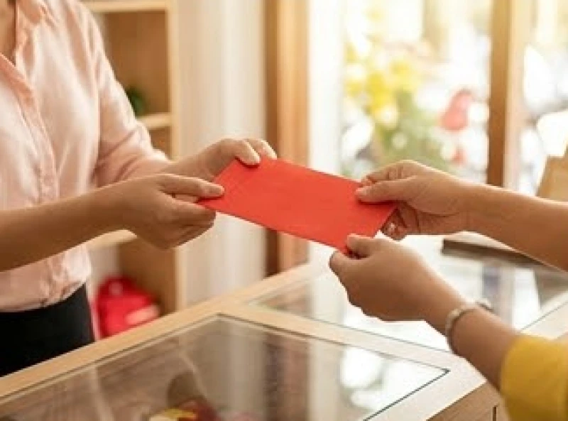 Chủ cửa hàng mỉm cười đưa phong bao lì xì màu đỏ rực rỡ cho vị khách vừa mua món hàng đầu tiên