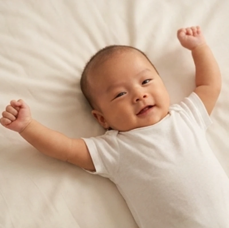 Bé trai sơ sinh khỏe mạnh đang vươn tay mạnh mẽ trên chiếc giường êm ái đại diện cho chí lớn và sự kiên cường