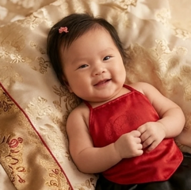 Bé gái sơ sinh mặc chiếc áo yếm lụa đỏ truyền thống đang tươi cười rạng rỡ tượng trưng cho sự phú quý đài các