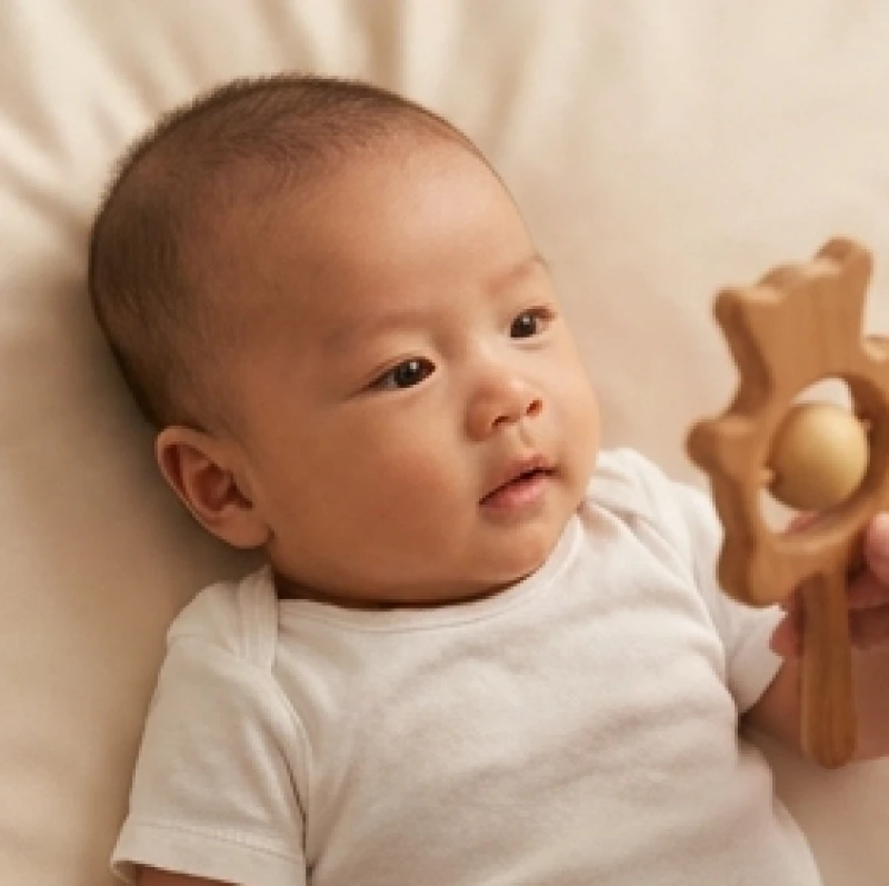 Em bé trai sơ sinh với ánh mắt sáng ngời và thông minh đang nhìn chăm chú vào đồ chơi bằng gỗ rất đáng yêu
