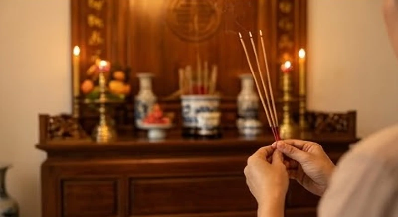 Gia chủ thành tâm chắp tay đứng trước bàn thờ gia tiên với ba nén nhang đang cháy để dâng lời xin lỗi