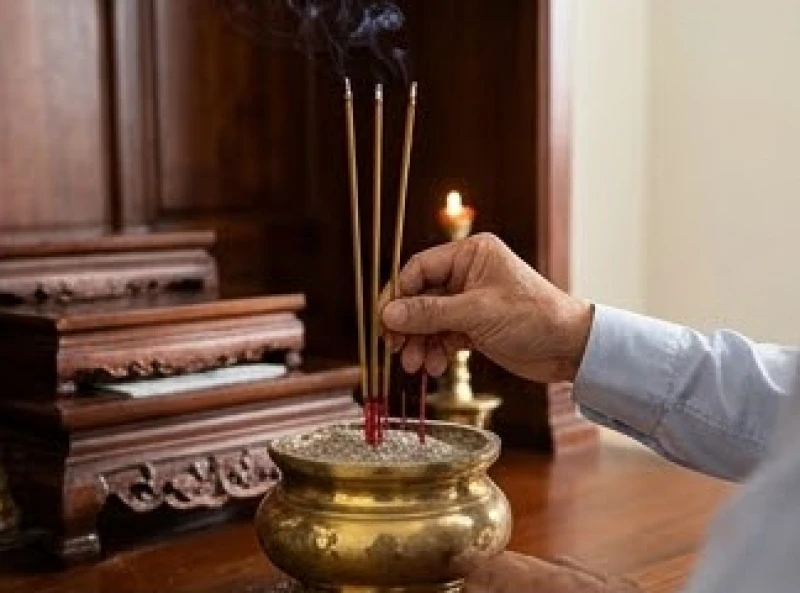 Nam gia chủ mặc áo sơ mi thắp ba nén nhang dâng lên bát hương Thổ Công trên bàn thờ gia tiên