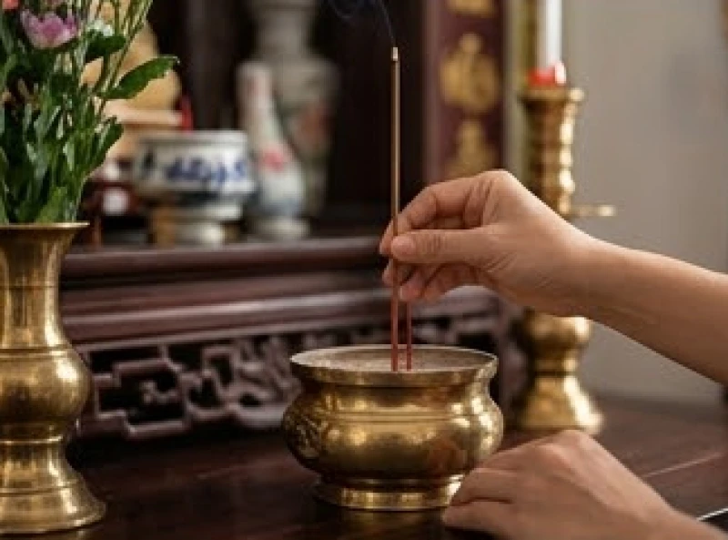 Bàn tay đang cắm nén nhang trầm vào bát hương trên bàn thờ gia tiên với sự thành kính
