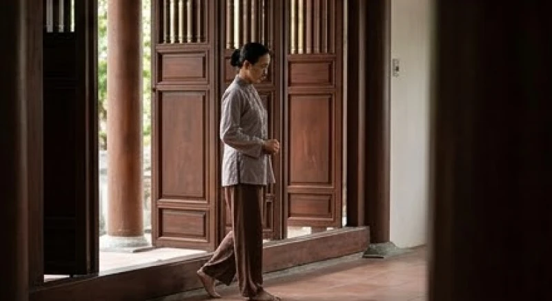 Người đi hành lễ mặc trang phục truyền thống kín đáo, màu xám nhạt, nhẹ nhàng bước qua ngưỡng cửa nhà chùa