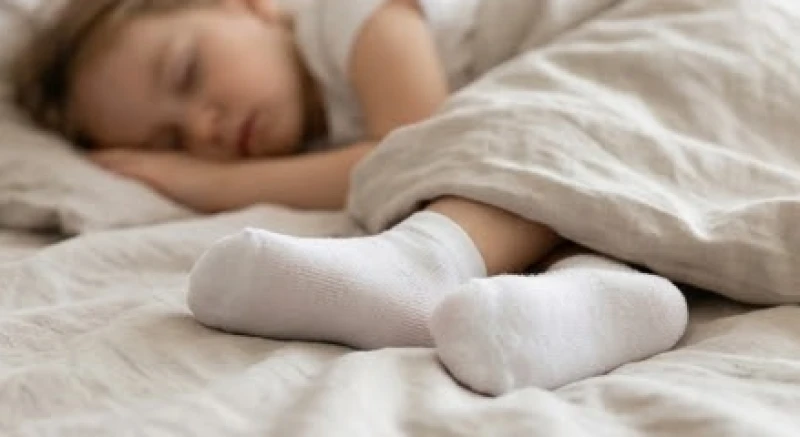 Em bé nằm ngủ ngoan trên giường với đôi bàn chân nhỏ nhắn mang tất cotton mỏng