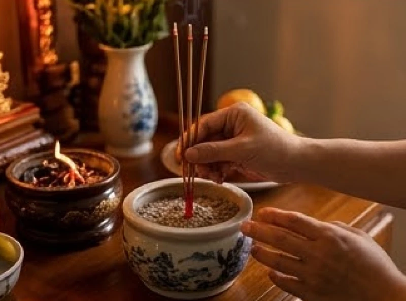 Bàn tay gia chủ cẩn thận cắm những nén nhang đầu tiên lên bát hương Thổ Công trước khi thắp cho Gia tiên