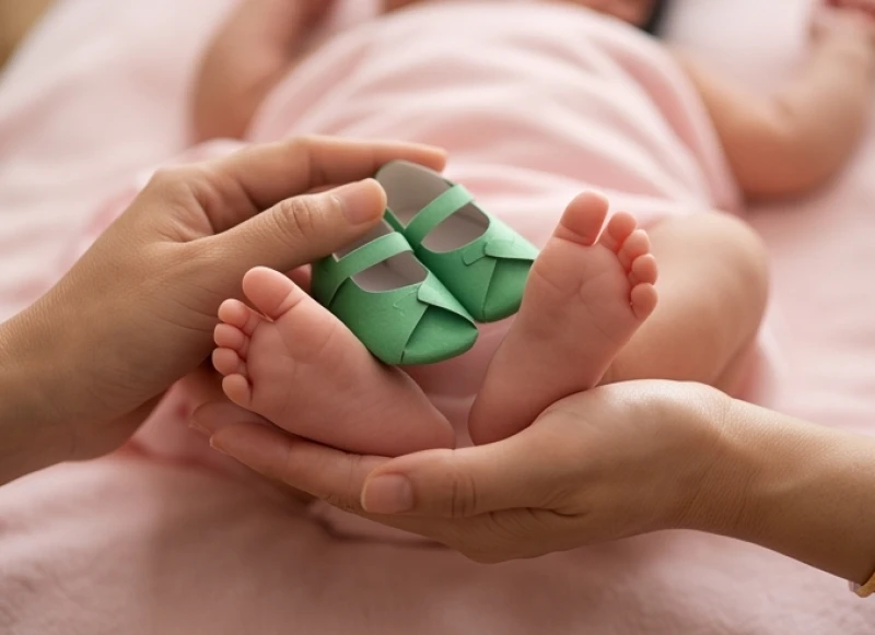 Bàn tay chạm nhẹ đôi hài giấy xanh vào gót chân nhỏ của em bé gái