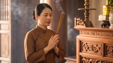 Người phụ nữ mặc áo dài truyền thống chắp tay thành kính dâng hương và đọc văn khấn Mẫu tại đền phủ uy nghiêm