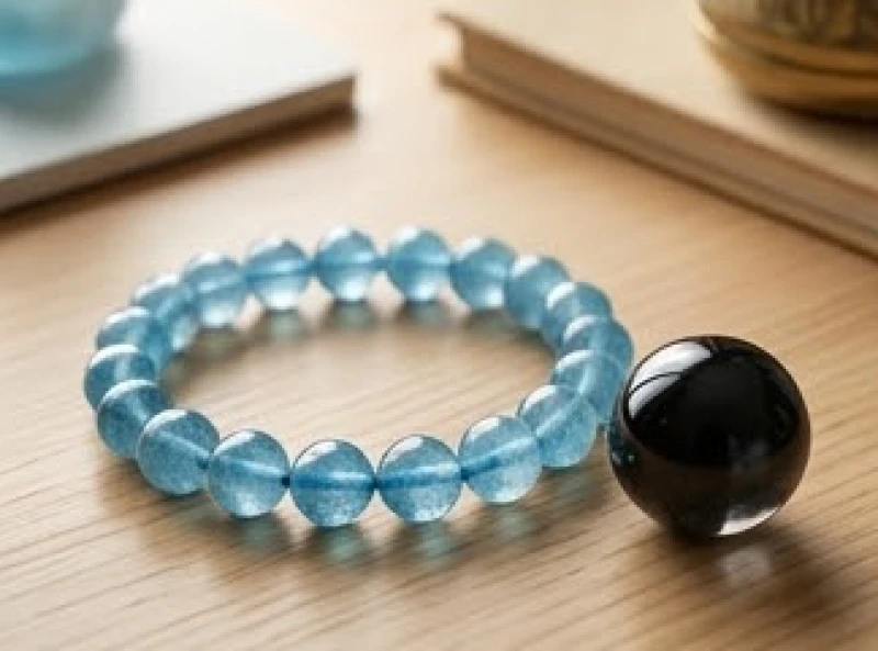 Vòng tay đá Aquamarine xanh biếc đặt cạnh quả cầu thạch anh đen trên bàn học