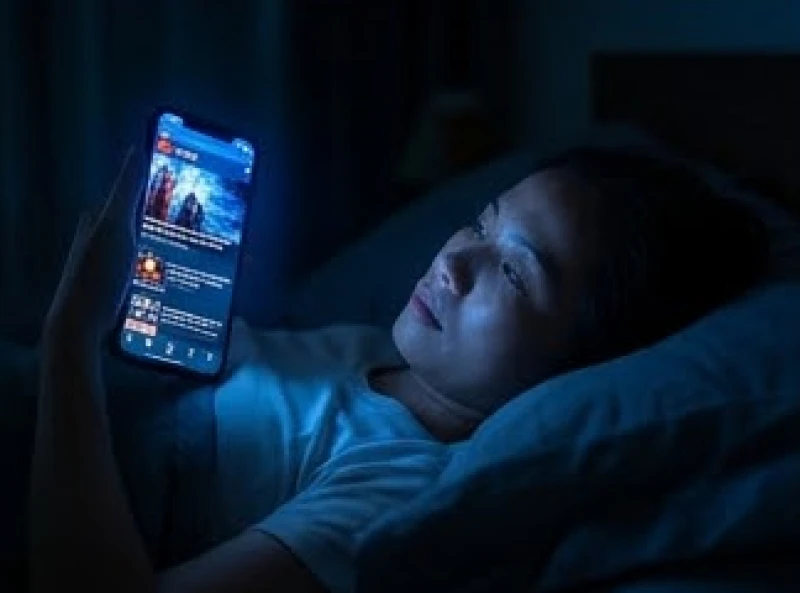 Một người lướt điện thoại đọc tin tức trong không gian tối tăm trước khi chìm vào giấc ngủ